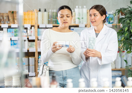 Middle-aged woman choosing ointment while pharmacist offering in drugstore Middle-aged woman choosing ointment while pharmacist offering in drugstore 142056145