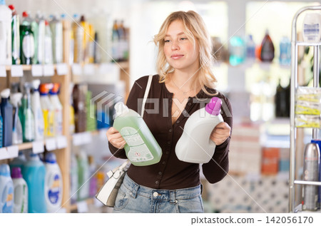 Girl housewife in household store examines goods, chooses liquid detergent Girl housewife in household store examines goods, chooses liquid detergent 142056170