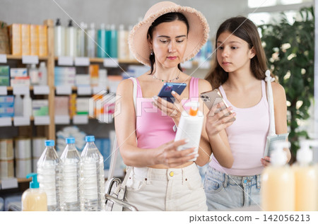 Focused family of adult woman and young girl scan QR code on label and choosing sunscreen cream or sun protection product and compare with other medicine in pharmacy Focused family of adult woman and young girl scan QR code on label and choosing sunscreen cream or sun protection product and compare with other medicine in pharmacy 142056213