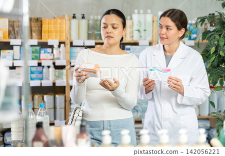 Middle-aged woman choosing pills in box while pharmacist offering in drugstore Middle-aged woman choosing pills in box while pharmacist offering in drugstore 142056221