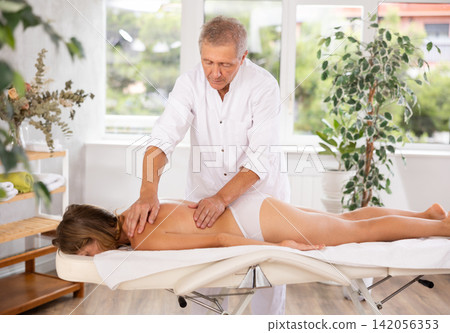 Skilled old masseur conducting back massage for woman client Skilled old masseur conducting back massage for woman client 142056353