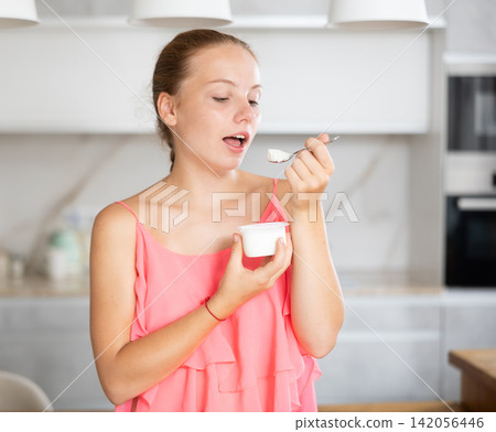 Teenage girl is eating yogurt in kitchen. Teenage girl is eating yogurt in kitchen. 142056446