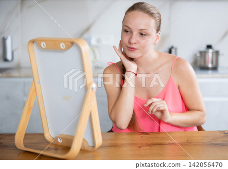 Happy teenage girl looking at her face in mirror in kitchen Happy teenage girl looking at her face in mirror in kitchen 142056470