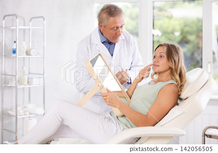 Middle-aged woman having consultation about face aesthetic while looking in the mirror Middle-aged woman having consultation about face aesthetic while looking in the mirror 142056505