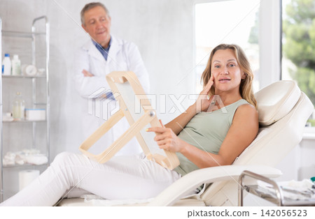 Happy woman examining her face after cosmetology procedures in clinic 142056523