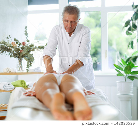 Skilled old masseur conducting back massage for woman client Skilled old masseur conducting back massage for woman client 142056559