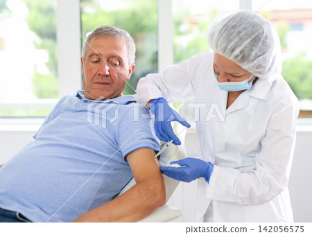 Woman doctor makes injection in arm of man Woman doctor makes injection in arm of man 142056575