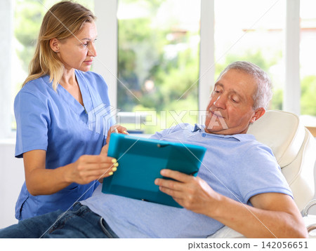 Old male patient signing papers while talking with woman doctor Old male patient signing papers while talking with woman doctor 142056651