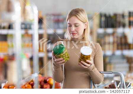 Girl buyer examine good, doubt and choose pickled olives in store Girl buyer examine good, doubt and choose pickled olives in store 142057117