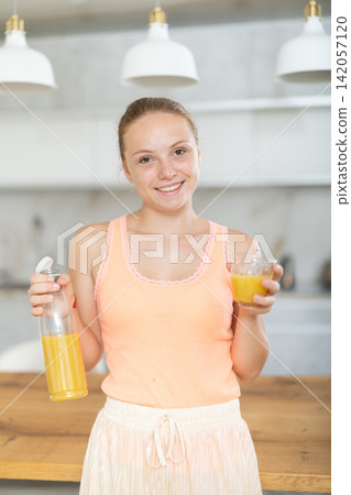 Teenage girl drinking fresh juice from glass in modern kitchen Teenage girl drinking fresh juice from glass in modern kitchen 142057120