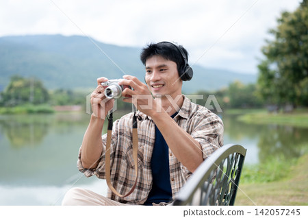 Young Asian Man Holding Camera Ready to Shoot Photo in Lakeside Park Young Asian Man Holding Camera Ready to Shoot Photo in Lakeside Park 142057245