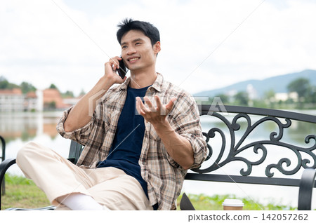 Young Asian Man Talking on Mobile Phone with Gestures in Park Young Asian Man Talking on Mobile Phone with Gestures in Park 142057262