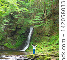 A woman gazes at the river flowing while looking at a waterfall. 142058033