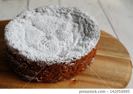 A diagonal composition of a whole chocolate cake placed on a wooden board. A diagonal composition of a whole chocolate cake placed on a wooden board. 142058995