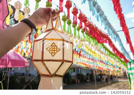 Woman's hand showing a traditional paper lantern during Yi peng (or Yee peng) festival in Wat Phra That Hariphunchai, Lamphun province, Thailand. Woman's hand showing a traditional paper lantern during Yi peng (or Yee peng) festival in Wat Phra That Hariphunchai, Lamphun province, Thailand. 142059152