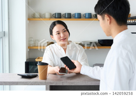 A man and a female store clerk pay using a smartphone. A man and a female store clerk pay using a smartphone. 142059258