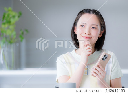 A housewife wearing an apron, holding her smartphone, thinks positively, ponders, considers choices, and so on. A housewife wearing an apron, holding her smartphone, thinks positively, ponders, considers choices, and so on. 142059463