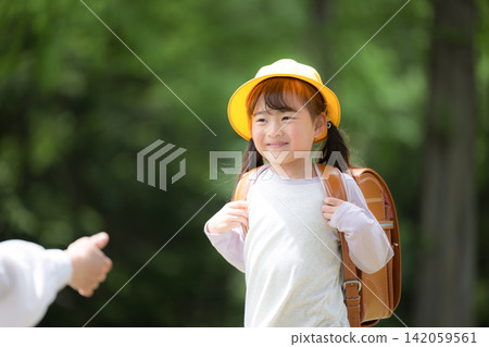 A cheerful girl with a schoolbag walks through the fresh greenery on her way to school; a first-grader wearing a yellow hat watches over her. A cheerful girl with a schoolbag walks through the fresh greenery on her way to school; a first-grader wearing a yellow hat watches over her. 142059561