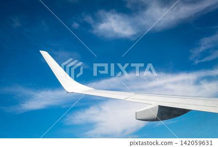 Commercial airplane wing seen from passenger window while flying above clouds under clear blue sky. Modern aviation, international flight, travel experience and tourism concept. Global tourism. Commercial airplane wing seen from passenger window while flying above clouds under clear blue sky. Modern aviation, international flight, travel experience and tourism concept. Global tourism. 142059631