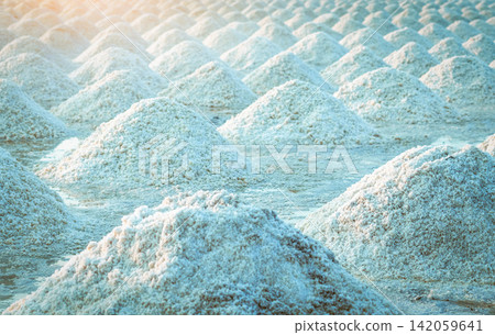 Sea salt piles in traditional salt farm during solar evaporation process for natural sodium chloride production and sustainable mineral harvesting in Thailand. Organic sea salt crystallization. Sea salt piles in traditional salt farm during solar evaporation process for natural sodium chloride production and sustainable mineral harvesting in Thailand. Organic sea salt crystallization. 142059641