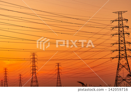 High voltage electricity transmission towers and power lines silhouetted against sunset sky. Electrical grid infrastructure, energy distribution, utility engineering and modern power networks. High voltage electricity transmission towers and power lines silhouetted against sunset sky. Electrical grid infrastructure, energy distribution, utility engineering and modern power networks. 142059716