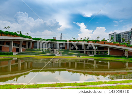 Modern sustainable campus architecture with green roof, reflection pond and dramatic blue sky, contemporary educational building featuring eco friendly landscape and minimalist architectural design. Modern sustainable campus architecture with green roof, reflection pond and dramatic blue sky, contemporary educational building featuring eco friendly landscape and minimalist architectural design. 142059828