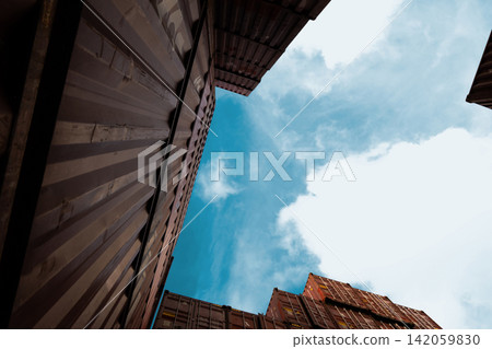 Low angle view between stacked shipping containers at international cargo terminal, modern logistics infrastructure supporting global freight transportation, import export and supply chain operations. Low angle view between stacked shipping containers at international cargo terminal, modern logistics infrastructure supporting global freight transportation, import export and supply chain operations. 142059830