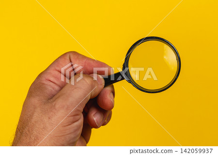 Hand holding a magnifying glass against a bright yellow background Hand holding a magnifying glass against a bright yellow background 142059937
