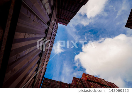 Low angle view between stacked shipping containers at international cargo terminal, modern logistics infrastructure supporting global freight transportation, import export and supply chain operations. Low angle view between stacked shipping containers at international cargo terminal, modern logistics infrastructure supporting global freight transportation, import export and supply chain operations. 142060323