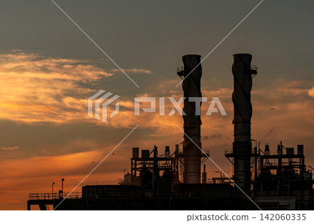 Silhouette natural gas power plant against dramatic orange sunset sky with industrial turbines and storage facilities. Modern electricity generation, energy security and sustainable infrastructure. Silhouette natural gas power plant against dramatic orange sunset sky with industrial turbines and storage facilities. Modern electricity generation, energy security and sustainable infrastructure. 142060335