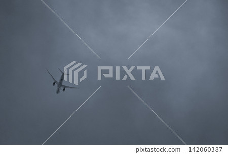 Commercial passenger airplane flying through dark storm clouds under an overcast sky. Aviation, air travel, challenging weather conditions, transportation safety and modern airline operations. Commercial passenger airplane flying through dark storm clouds under an overcast sky. Aviation, air travel, challenging weather conditions, transportation safety and modern airline operations. 142060387