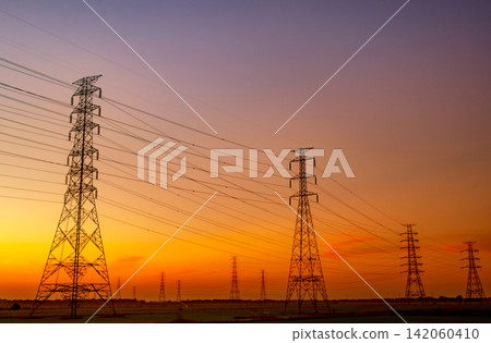 High voltage electricity transmission towers stretching across rural landscape beneath sunset sky. National power grid infrastructure, electrical engineering, energy distribution and utility network. High voltage electricity transmission towers stretching across rural landscape beneath sunset sky. National power grid infrastructure, electrical engineering, energy distribution and utility network. 142060410