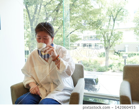 盛夏時節,一位中年女上班族在辦公大樓的休息室休息喝咖啡。 盛夏時節,一位中年女上班族在辦公大樓的休息室休息喝咖啡。 142060455
