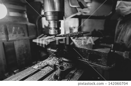 Milling machine working near worker with a protective mask. Tool for cut metal workpiece. Vertical milling machine with cemented carbide milling cutter. Steel manufacturing industry. Milling process. Milling machine working near worker with a protective mask. Tool for cut metal workpiece. Vertical milling machine with cemented carbide milling cutter. Steel manufacturing industry. Milling process. 142060704