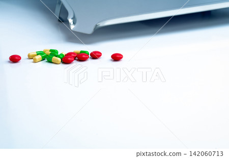 Red round sugar coated tablets and green-yellow capsules with stainless steel drug tray on white table. Pharmaceutics concept. Pharmaceutical industry. Pharmacy products. Healthcare and medication. Red round sugar coated tablets and green-yellow capsules with stainless steel drug tray on white table. Pharmaceutics concept. Pharmaceutical industry. Pharmacy products. Healthcare and medication. 142060713