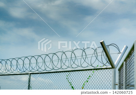 Prison security fence. Barbed wire security fence. Razor wire jail fence. Barrier border. Boundary security wall. Prison for arrest criminals or terrorists. Private area. Military zone concept. Prison security fence. Barbed wire security fence. Razor wire jail fence. Barrier border. Boundary security wall. Prison for arrest criminals or terrorists. Private area. Military zone concept. 142060725