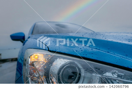 Blue passenger car covered with raindrops beneath a rainbow after rainfall, representing hope, safe transportation, weather change, recovery, resilience and new beginnings after the storm. Blue passenger car covered with raindrops beneath a rainbow after rainfall, representing hope, safe transportation, weather change, recovery, resilience and new beginnings after the storm. 142060796