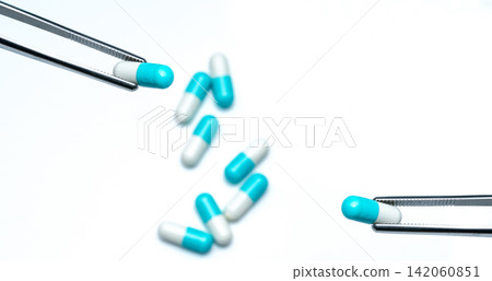 Forceps pick white-blue capsule from group of capsule pills. Drugs choose. Antibiotic drug selection. Antibiotic drug resistance concept. QA and QC in pharmaceutical factory concept. Drugs of choice. Forceps pick white-blue capsule from group of capsule pills. Drugs choose. Antibiotic drug selection. Antibiotic drug resistance concept. QA and QC in pharmaceutical factory concept. Drugs of choice. 142060851