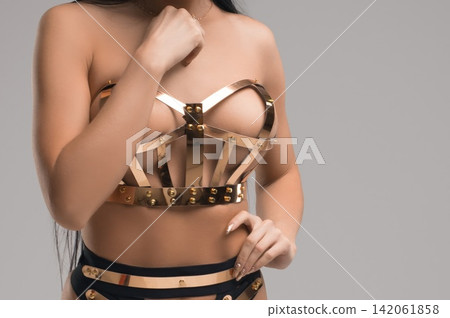 Woman in shiny gold metal lingerie stands in studio Woman in shiny gold metal lingerie stands in studio 142061858