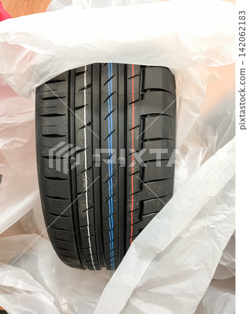 New black summer tire with colorful tread stripes unwrapped from plastic packaging New black summer tire with colorful tread stripes unwrapped from plastic packaging 142062183