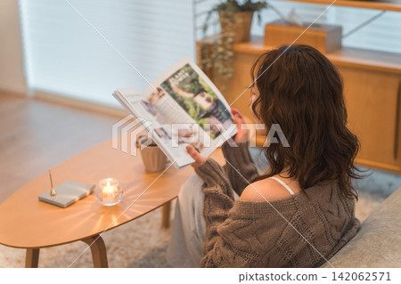 A stylish Asian woman sitting in the living room at night, reading a magazine. A stylish Asian woman sitting in the living room at night, reading a magazine. 142062571