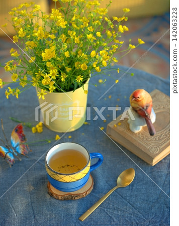 A ceramic blue cup with tea and yellow wildflowers. A blue and light blue color palette. A ceramic blue cup with tea and yellow wildflowers. A blue and light blue color palette. 142063228