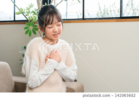 A girl in elementary and middle school sitting on a sofa at home holding her chest due to chest pain A girl in elementary and middle school sitting on a sofa at home holding her chest due to chest pain 142063682