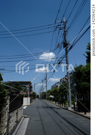 A scene of utility poles and wiring in a residential area, against a blue sky. A scene of utility poles and wiring in a residential area, against a blue sky. 142064214