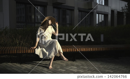 Woman in sun hat sitting on an outdoor bench Woman in sun hat sitting on an outdoor bench 142064766