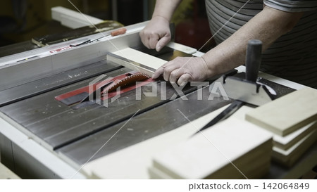Woodworking Process Detailed. Craftsman Carefully Pushing Timber Toward Cutting Blade For Accuracy. Media Woodworking Process Detailed. Craftsman Carefully Pushing Timber Toward Cutting Blade For Accuracy. Media 142064849
