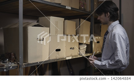 Warehouse worker checking inventory on storage shelves 142064884