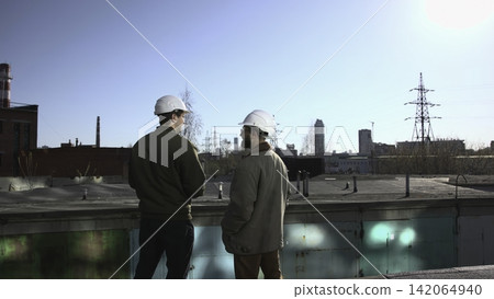 Two Experts Diligently Examine Parapets And Towers Against Industrial Backdrop With Professionalism. Media Two Experts Diligently Examine Parapets And Towers Against Industrial Backdrop With Professionalism. Media 142064940