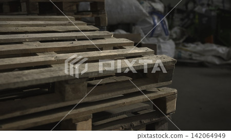 Rough Timber Storage. Wooden Pallets In Industrial Setting. Dim Warehouse With Stacked Wooden Shipping Pallets. Media 142064949