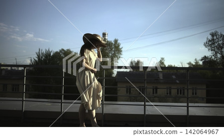 Woman in a sun hat standing on a rooftop balcony in summer light Woman in a sun hat standing on a rooftop balcony in summer light 142064967